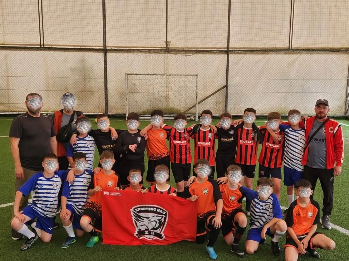The Sporting Has team together on the pitch: around twenty children and teenagers in kit, with two coaches, holding the project's banner